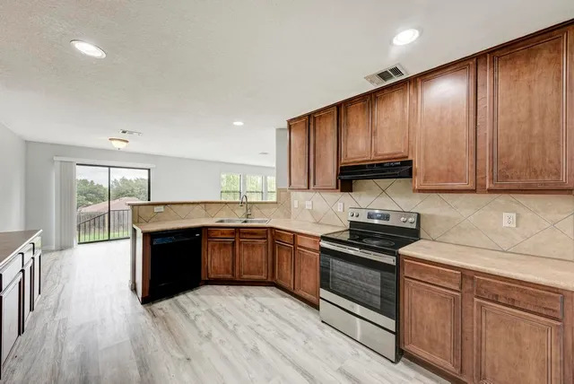 a kitchen with stainless steel appliances granite countertop a refrigerator a stove and a sink with wooden floor
