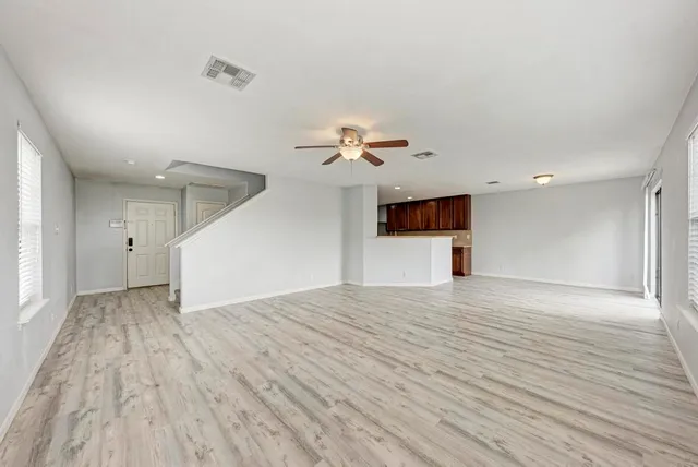 a view of an empty room with wooden floor and a ceiling fan