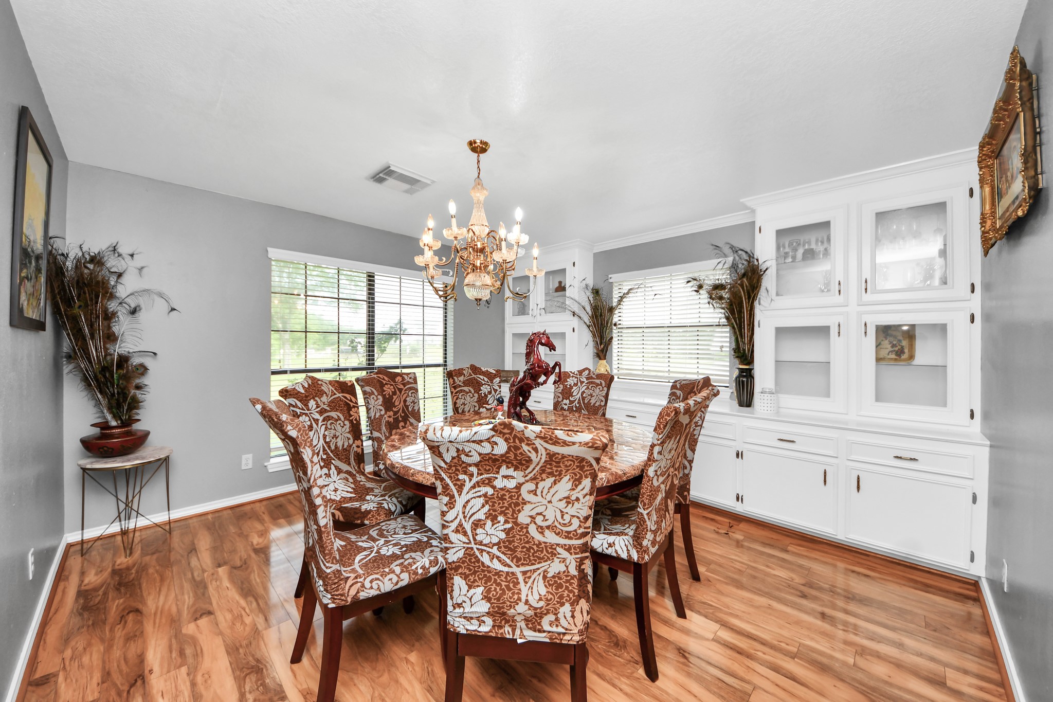 12746 Roy Road Pearland, TX 77581 - Photo 25 of 47 This dining room features elegant wood flooring, a large window for natural light, and a classic chandelier. It includes built-in white cabinetry and a spacious dining table with upholstered chairs, offering both style and functionality.