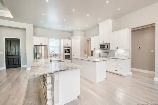 a large white kitchen with stainless steel appliances kitchen island granite countertop a large counter top and white cabinets