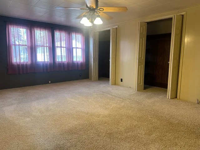 an empty room with windows and chandelier fan