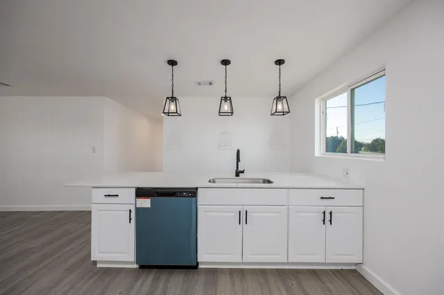 a view of a kitchen with a sink and dishwasher a stove top oven with wooden floor