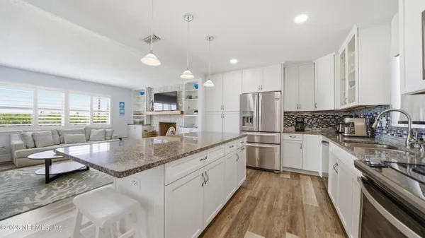 a kitchen with stainless steel appliances granite countertop a stove top oven a sink dishwasher a refrigerator and white cabinets with wooden floor