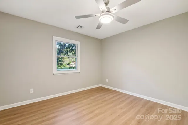 an empty room with wooden floor chandelier fan and windows