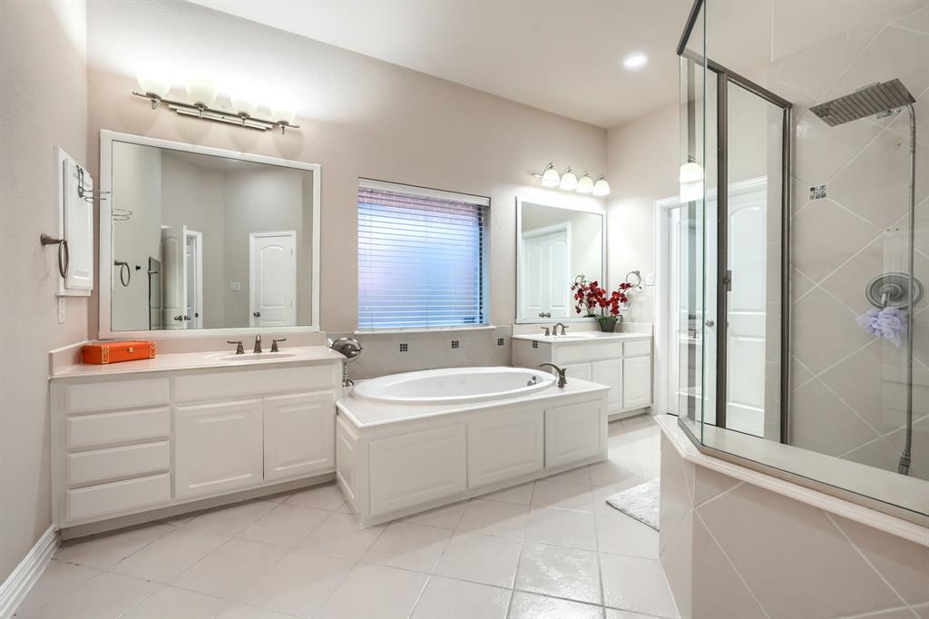 2246 Longview Road Irving, TX 75063 - Photo 21 of 40 Spacious bathroom featuring a built-in soaking tub, dual vanities with white cabinetry, a glass-enclosed shower, and light-toned tile flooring