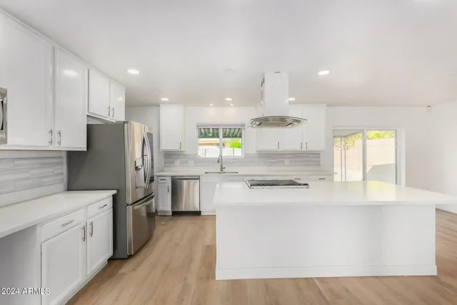 a kitchen with stainless steel appliances kitchen island granite countertop a stove a sink a refrigerator and white cabinets with wooden floor