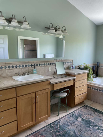 7030 West 2100 North Mendon, UT 84325 - Photo 37 of 67 Bathroom featuring an extended vanity with wood-finish cabinetry and integrated makeup desk, a drop-in sink, and a tiled countertop with decorative accent trim