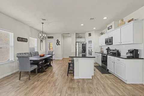 a kitchen with stainless steel appliances kitchen island granite countertop a stove a sink a refrigerator and white cabinets with wooden floor
