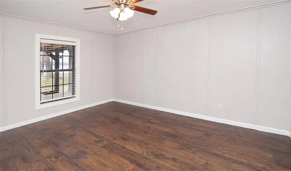an empty room with wooden floor chandelier fan and windows