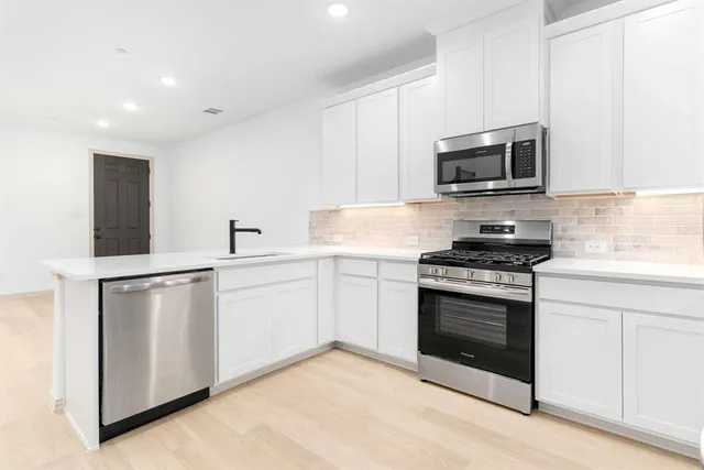 a kitchen with stainless steel appliances white cabinets a sink stove and microwave