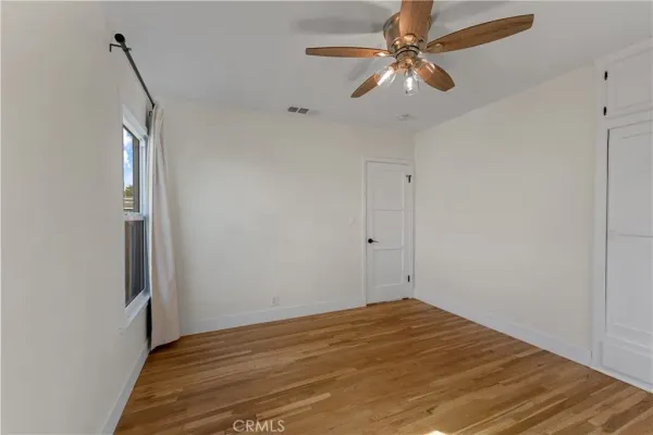 a view of empty room with wooden floor and fan