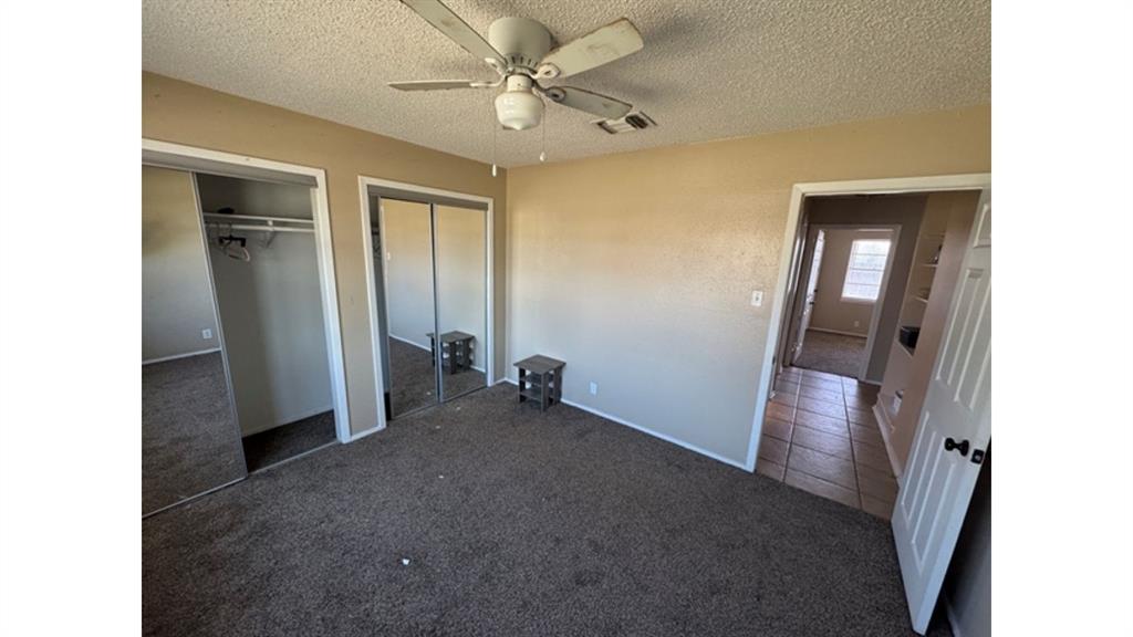 4004 Vicky Street Big Spring, TX 79720 - Photo 18 of 37 Unfurnished bedroom with dark carpet, two closets, ceiling fan, and a textured ceiling