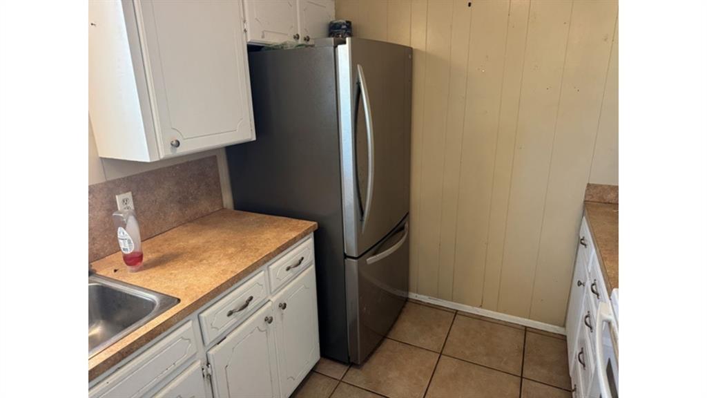 4004 Vicky Street Big Spring, TX 79720 - Photo 28 of 37 Kitchen featuring wood walls, white cabinetry, light tile patterned flooring, light countertops, and freestanding refrigerator