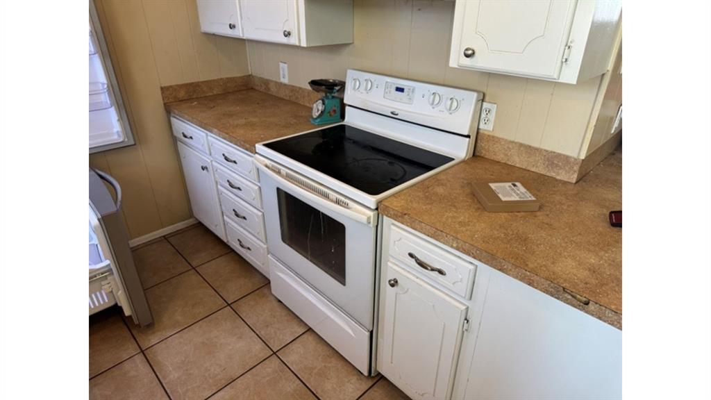 4004 Vicky Street Big Spring, TX 79720 - Photo 29 of 37 Kitchen with white electric stove, white cabinetry, light tile patterned flooring, and dark countertops