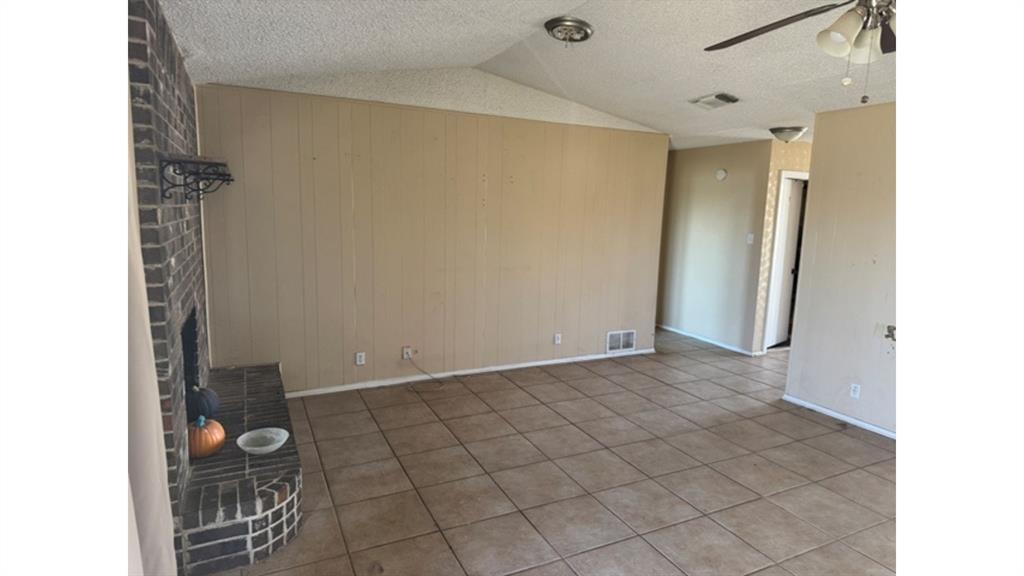 4004 Vicky Street Big Spring, TX 79720 - Photo 31 of 37 Unfurnished living room featuring ceiling fan, a brick fireplace, tile patterned floors, and wood walls