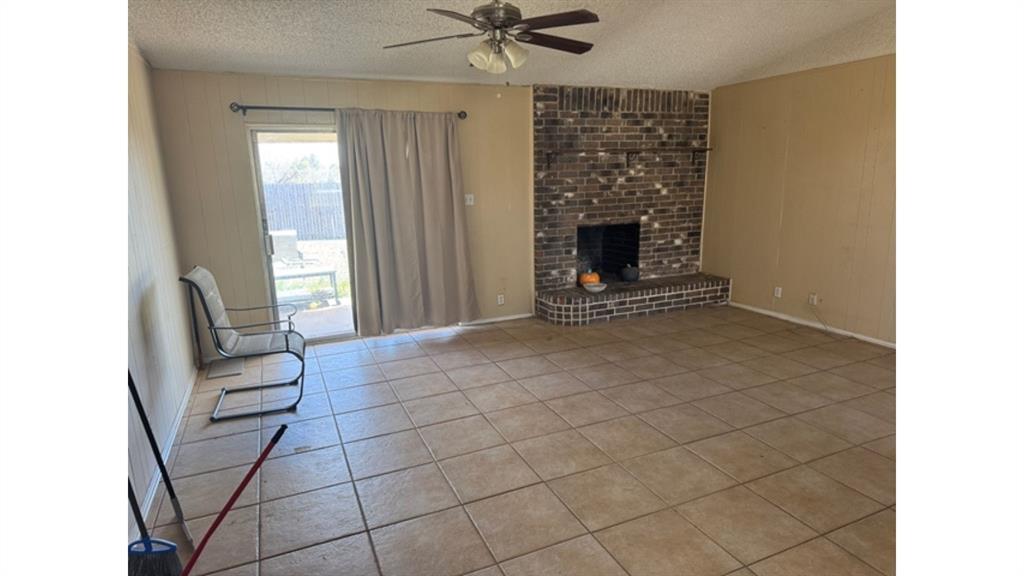 4004 Vicky Street Big Spring, TX 79720 - Photo 33 of 37 Unfurnished living room with wood walls, ceiling fan, light tile patterned flooring, a fireplace, and a textured ceiling