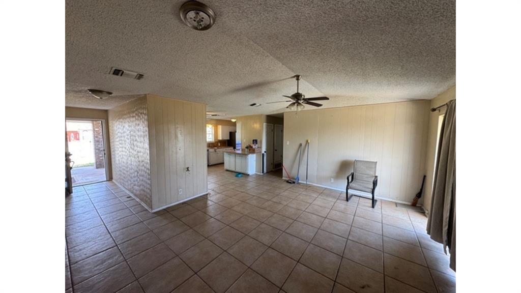 4004 Vicky Street Big Spring, TX 79720 - Photo 34 of 37 Unfurnished living room with dark tile patterned flooring, a textured ceiling, ceiling fan, and wooden walls
