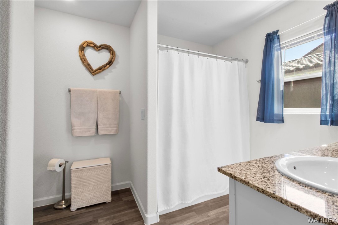 2424 Granite Road Bullhead City, AZ 86442 - Photo 23 of 50 Bathroom featuring a shower with a white curtain, a window with blue curtains, wood-finish flooring, a vanity with a granite-style countertop, and a built-in sink