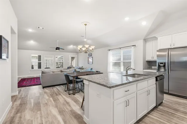 a kitchen with stainless steel appliances granite countertop a sink dishwasher and white cabinets with wooden floor