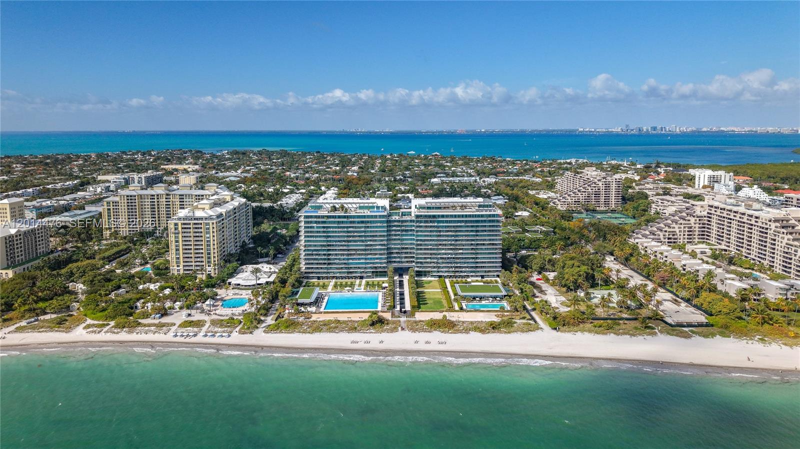 360 Ocean Drive, Unit 1106S Key Biscayne, FL 33149 - Photo 52 of 67 Aerial Community View – A broad overhead perspective frames the building within its coastal setting, with Biscayne Bay, nearby residences, and the skyline visible in the distance. The composition highlights the scale of the property and its surrounding island landscape.