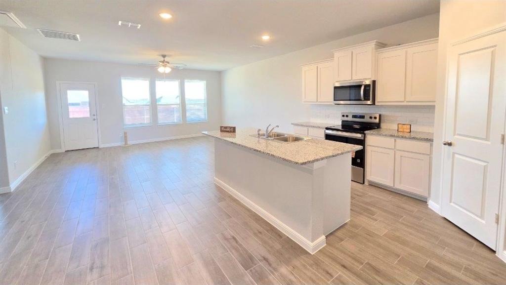 a kitchen with stainless steel appliances granite countertop a stove top oven a sink dishwasher a refrigerator and white cabinets with wooden floor