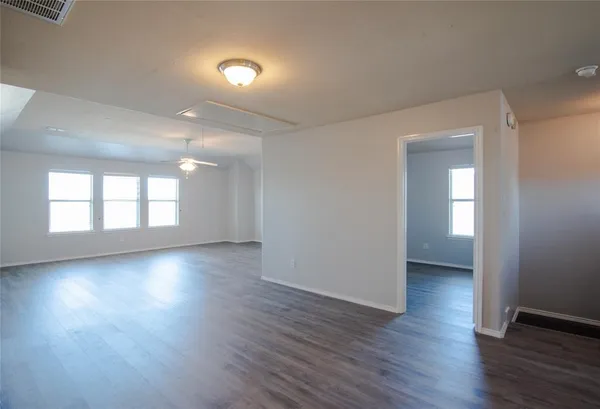 a view of an empty room with wooden floor and a ceiling fan