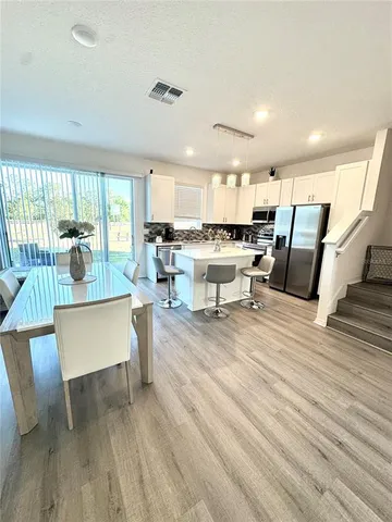 a room with stainless steel appliances a dining table wooden floor and a view of kitchen