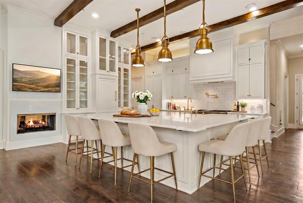 6900 Rockingham Court Colleyville, TX 76034 - Photo 10 of 40 Gourmet Chef's kitchen featuring a large central island with white cabinetry, wood flooring, exposed ceiling beams, and a modern fireplace, Sub Zero Refrigerator and Freezer, Updated Appliances, Dual Dishwashers. Ai staged.