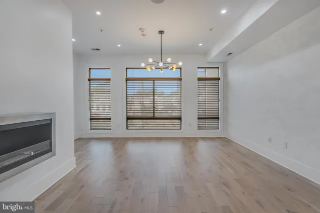 a view of an empty room with wooden floor and kitchen view