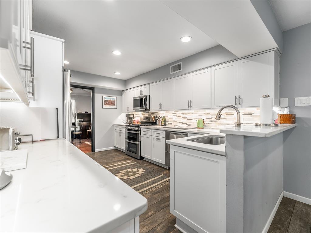 4446 Thunder Road Dallas, TX 75244 - Photo 12 of 39 Kitchen featuring stainless steel appliances, white cabinetry, decorative backsplash, dark wood-style flooring, and light stone countertops
