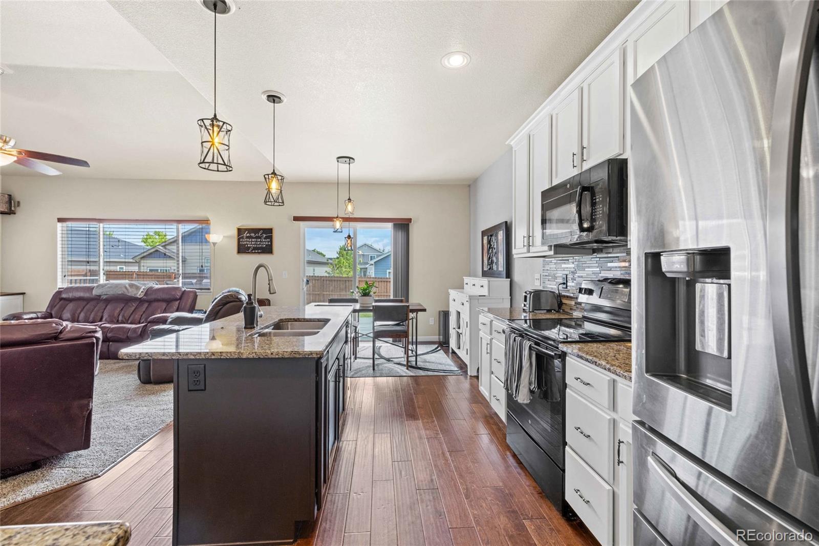 1030 Wagon Train Drive Milliken, CO 80543 - Photo 12 of 49 a kitchen with stainless steel appliances kitchen island granite countertop a refrigerator a stove top oven a sink dishwasher and white cabinets with wooden floor
