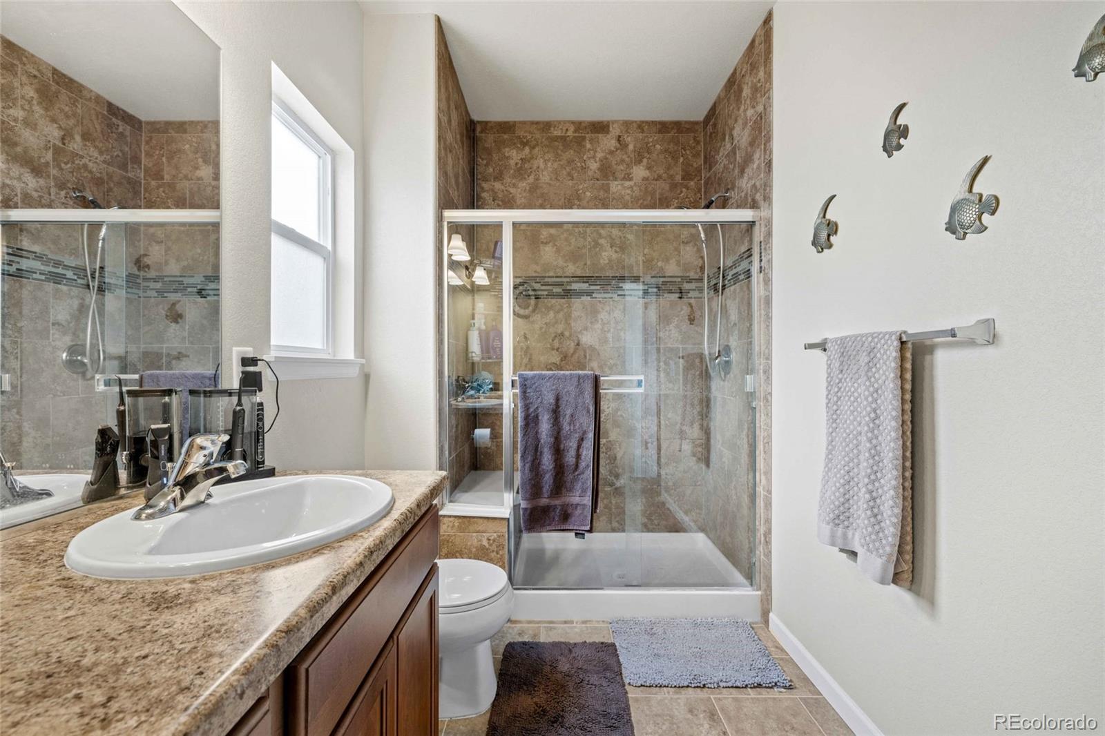 1030 Wagon Train Drive Milliken, CO 80543 - Photo 23 of 49 a bathroom with a granite countertop sink a mirror and shower