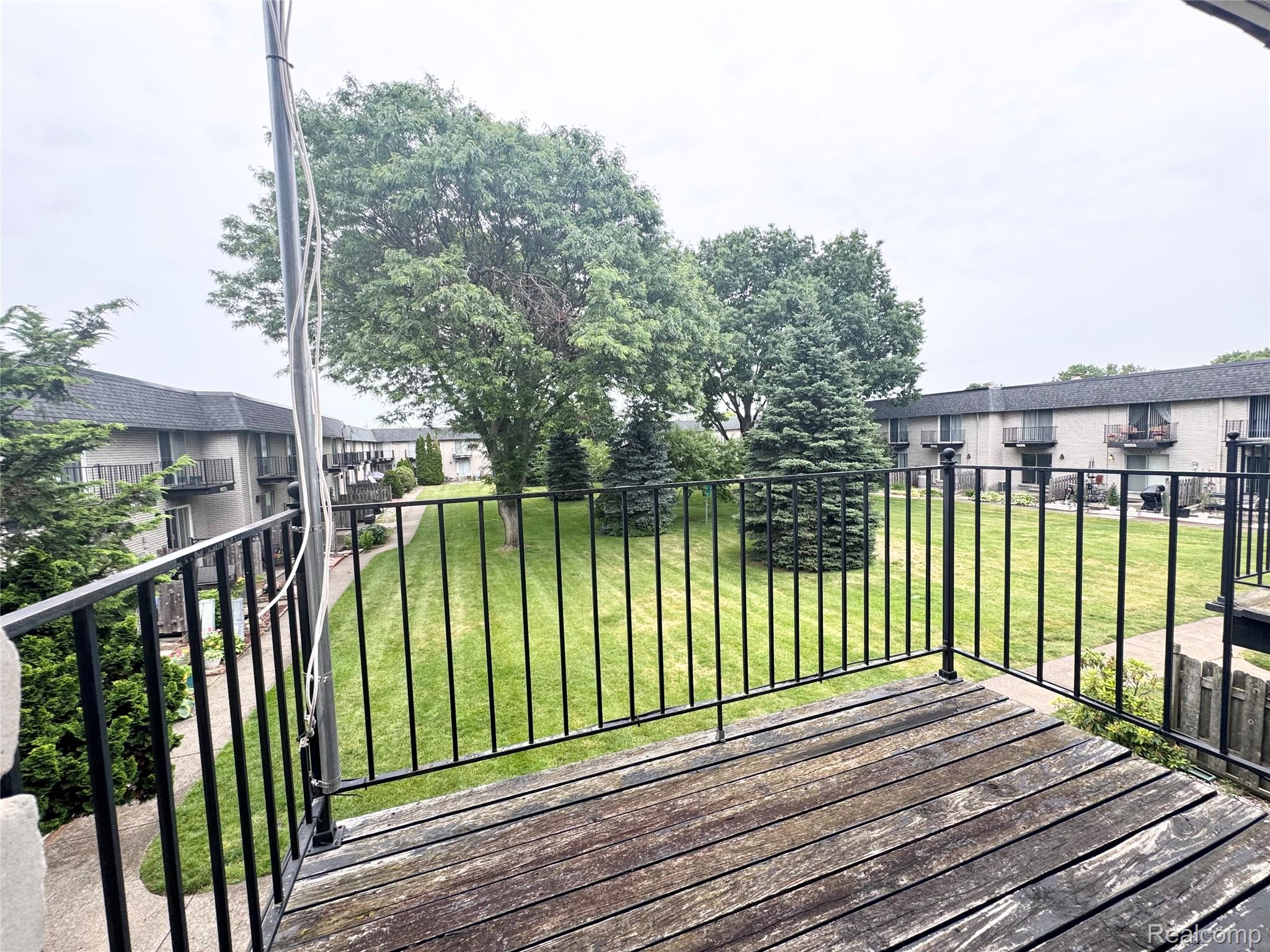 4386 15 Mile Road, Unit 64 Sterling Heights, MI 48310 - Photo 23 of 23 Private balcony with wood-finish flooring and black metal railings overlooking a central green space