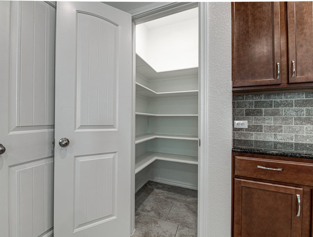 1237 Volente Lane Leander, TX 78641 - Photo 7 of 22 Ample storage solutions abound with a generous pantry featuring built-in shelving, complemented by rich cabinetry and a tiled backsplash.
