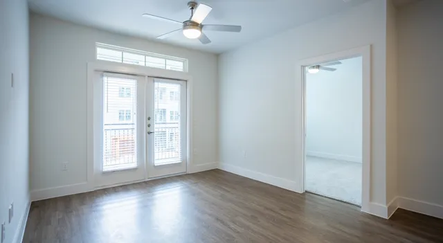 an empty room with wooden floor chandelier fan and windows