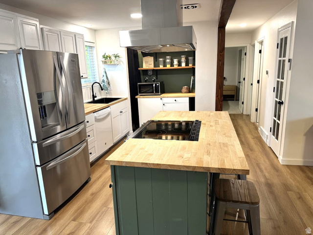1791 West 170 South, Unit 8 Provo, UT 84601 - Photo 5 of 25 Modern kitchen featuring a central island with an integrated cooktop, butcher block countertops, white cabinetry, stainless steel appliances, and wood-finish flooring
