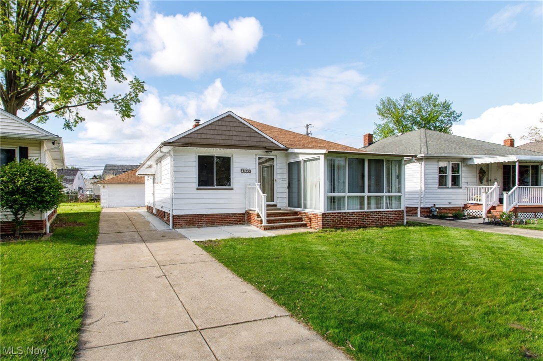 View of front facade featuring a front yard, a sunroom, and a detached garage