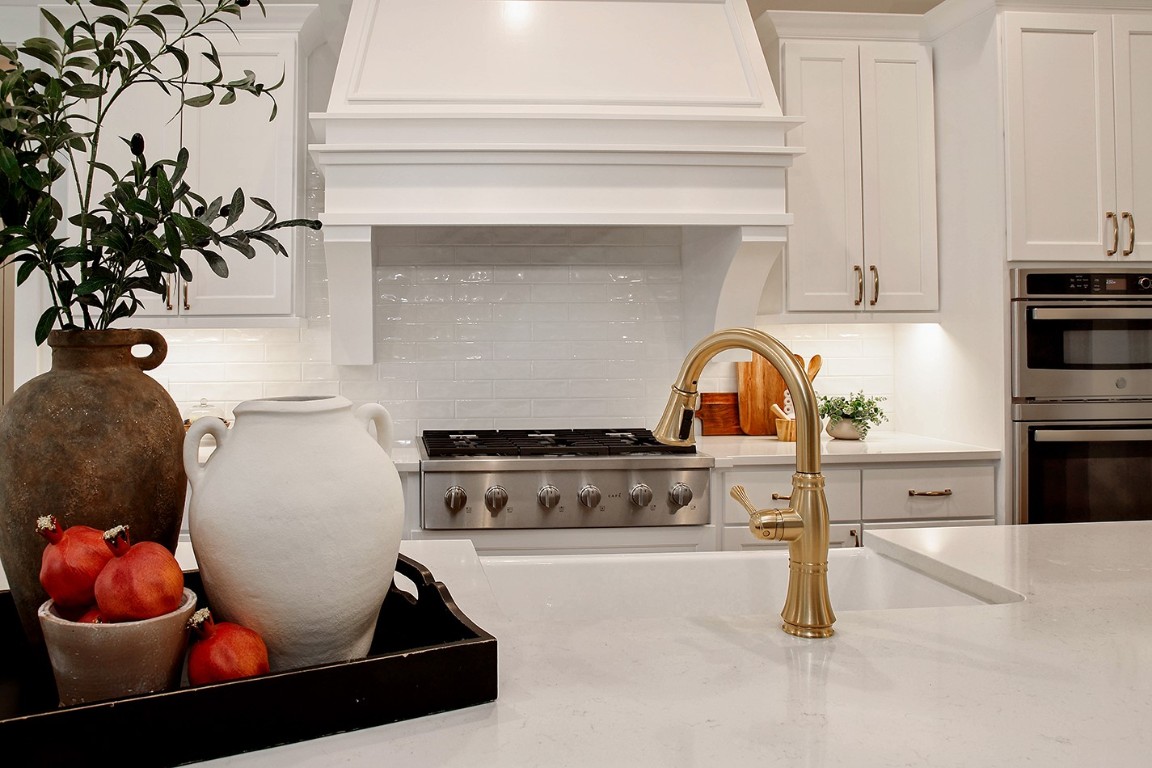 11709 Grand N Road Willis, TX 77378 - Photo 12 of 37 White cabinetry, white quartz counters and white tile backsplash in gloss finish all complement each other due to different tones, textures and finishes. Stainless steel gas cooktop with vent hood enclosed in custom cabinetry and built in double ovens are the perfect selection in this upscale kitchen, topped with the golden faucet.