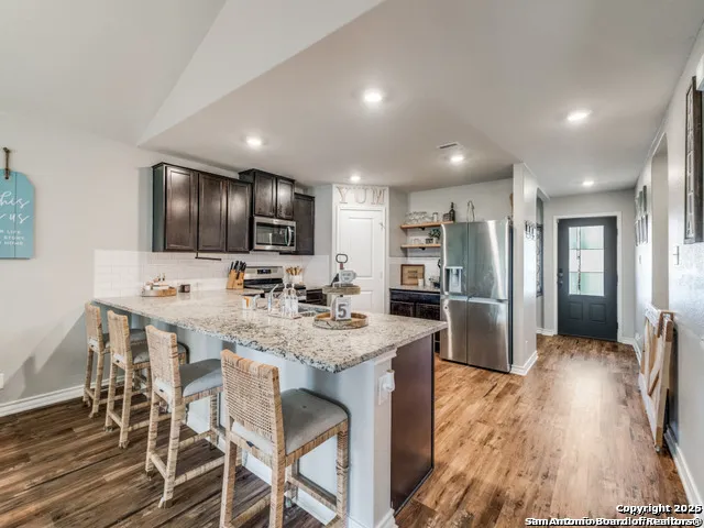 a kitchen with stainless steel appliances granite countertop a refrigerator a sink dishwasher a stove and a refrigerator with wooden floor