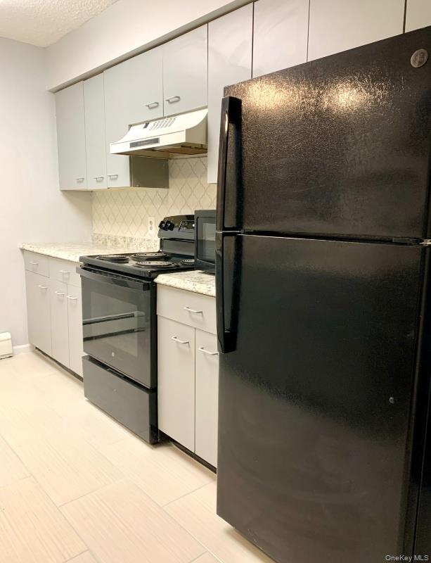 20 Fox Ridge Woodridge, NY 12789 - Photo 9 of 24 Kitchen with black appliances, under cabinet range hood, white cabinetry, backsplash, and a textured ceiling