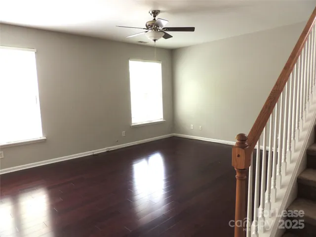 an empty room with wooden floor chandelier fan and windows