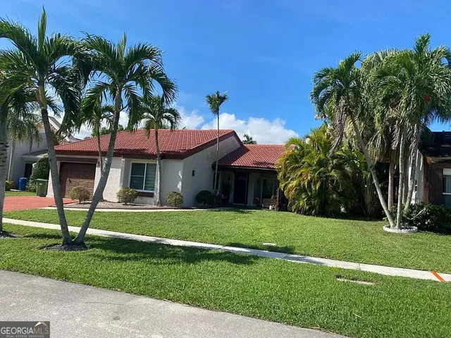 a view of a white house with a big yard and potted plants and palm trees