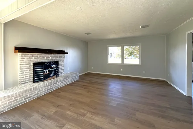 an empty room with wooden floor fireplace and windows