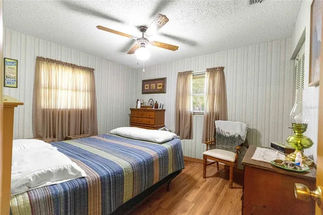 a bedroom with a bed table chair and two windows