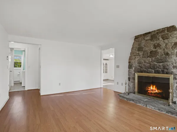 a view of an empty room with wooden floor fireplace and a window