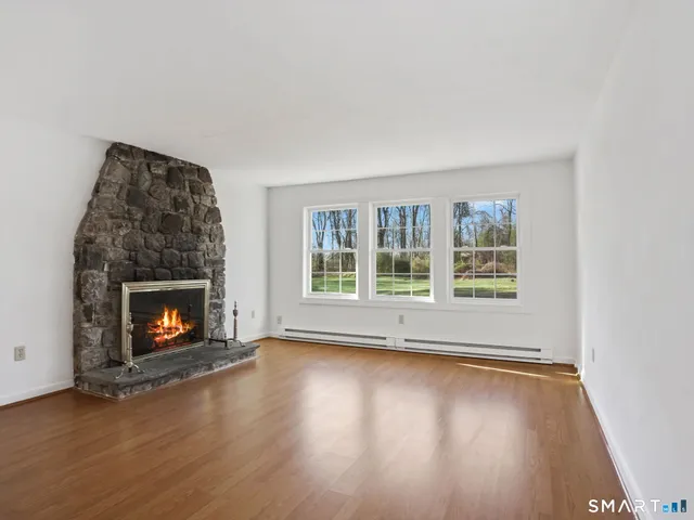 an empty room with wooden floor fire place and windows