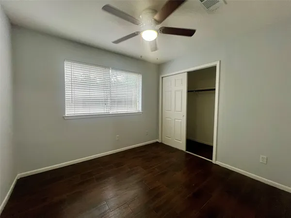 an empty room with wooden floor chandelier fan and windows