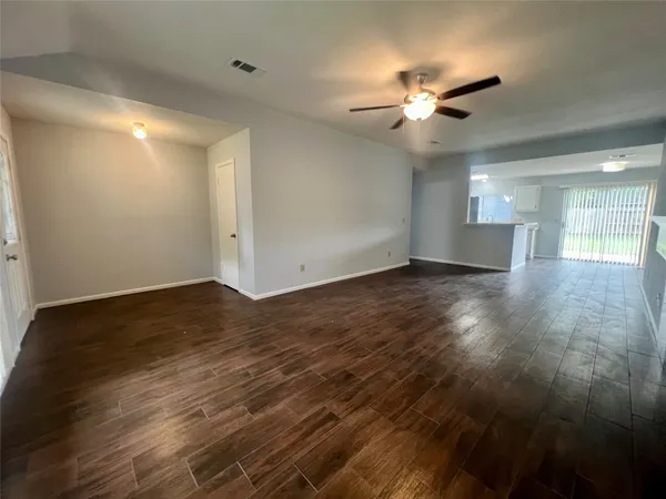 a view of an empty room with wooden floor and a ceiling fan