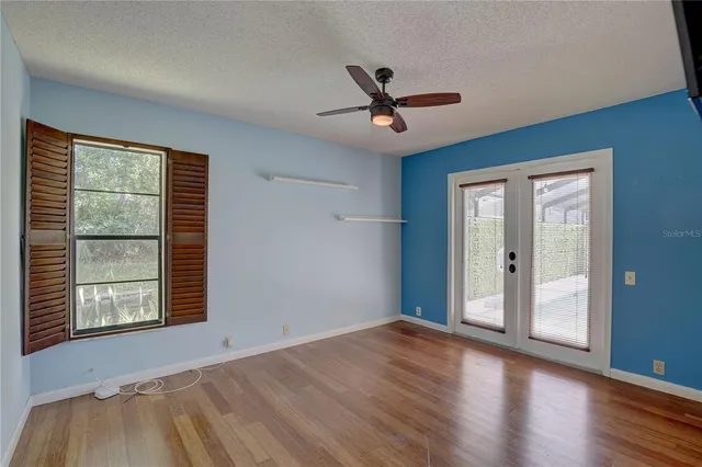 a view of a livingroom with wooden floor a ceiling fan and windows