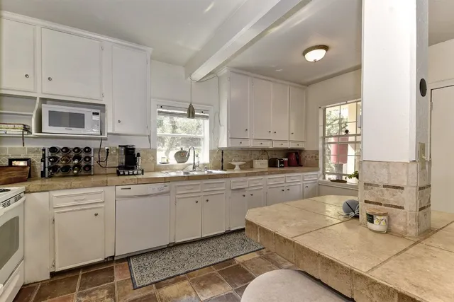 a white kitchen with granite countertop white cabinets sink and stove